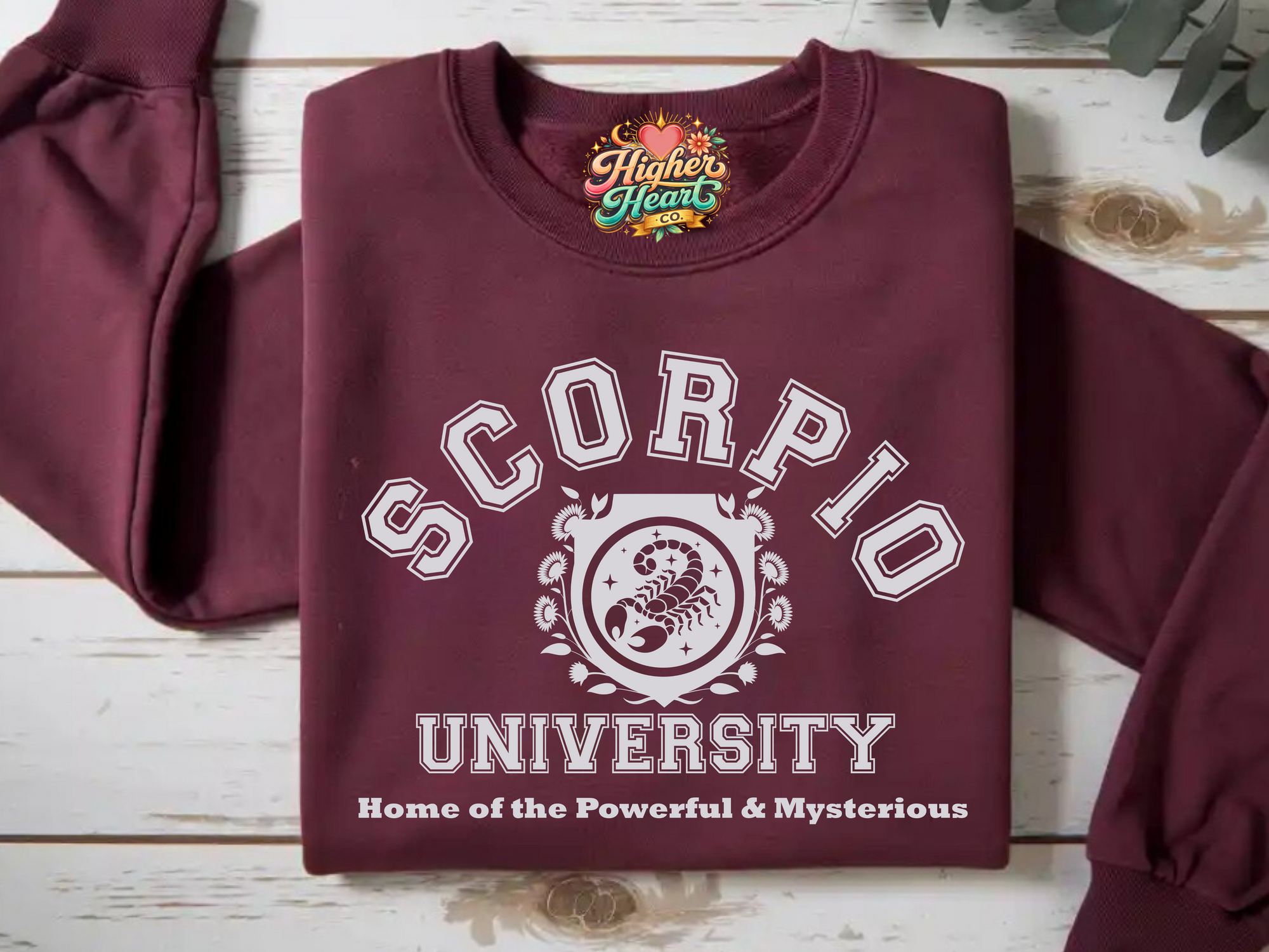 Maroon sweatshirt with 'Scorpio University' design on a wooden surface